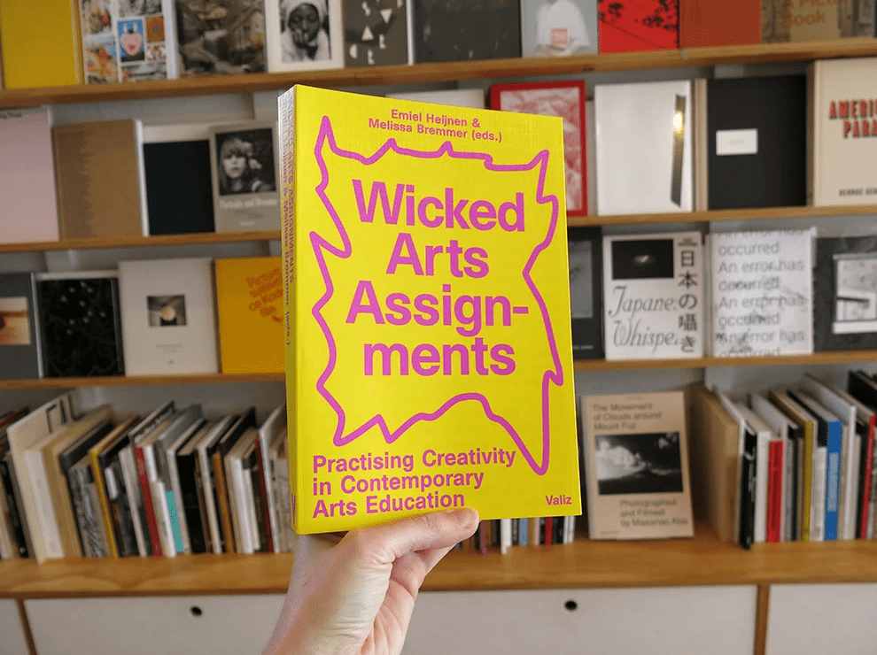 Boek Wicked Arts Assignments die vastgehouden wordt voor een boekenkast.
